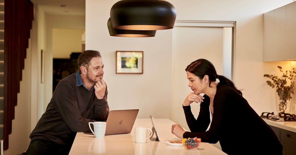 Man and woman sitting together in a kitchen, looking at the same screen