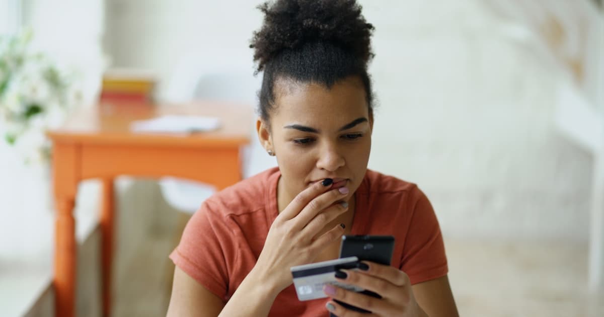 Woman looking at her phone with credit card in hand, managing her finances