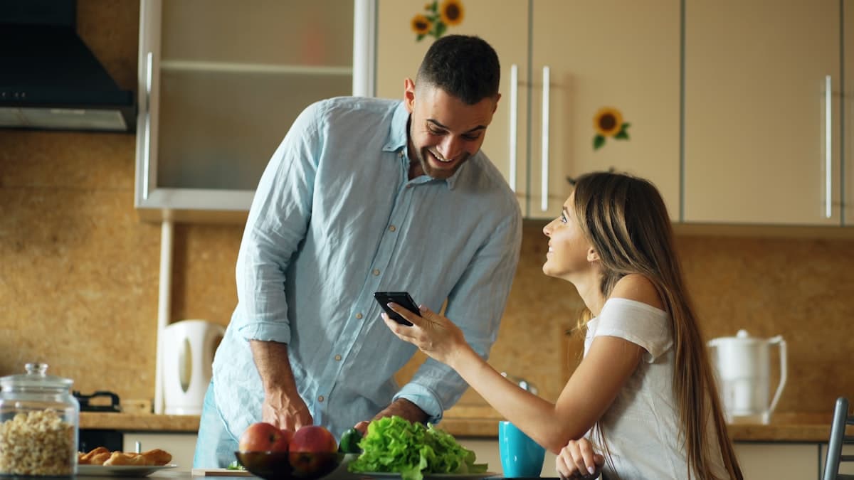 A couple looking at a phone together in a bright kitchen, relaxed