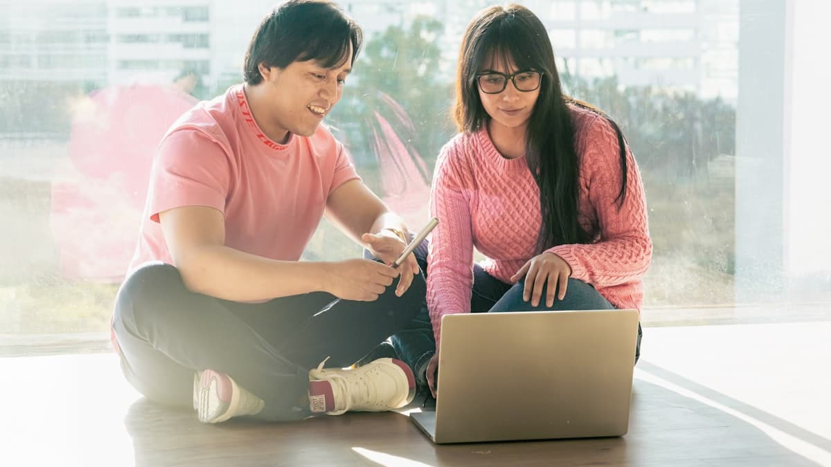 A man and woman sitting on the floor together, looking at a laptop screen