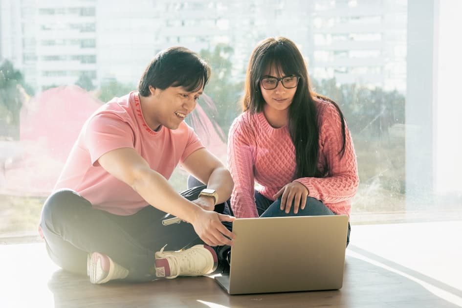 man and woman sitting on the floor looking at a laptop together