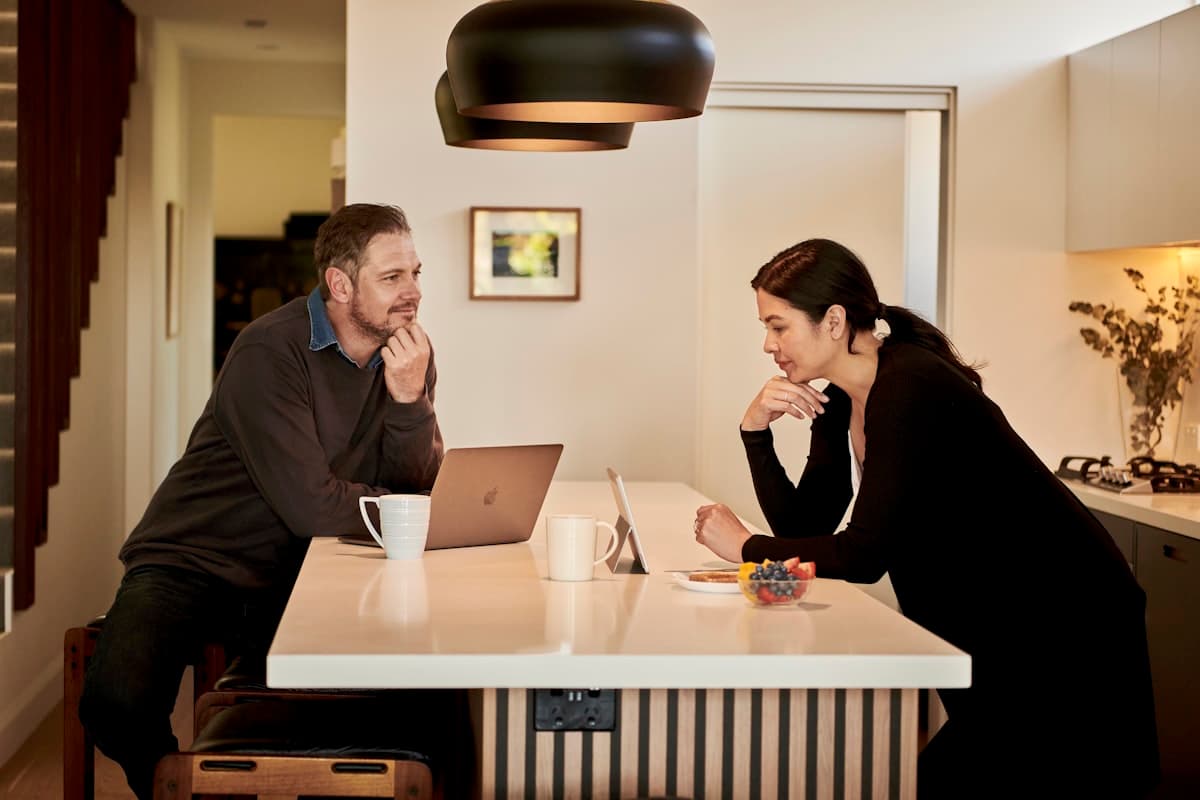 A man and woman sitting together in a kitchen, looking at something on a screen