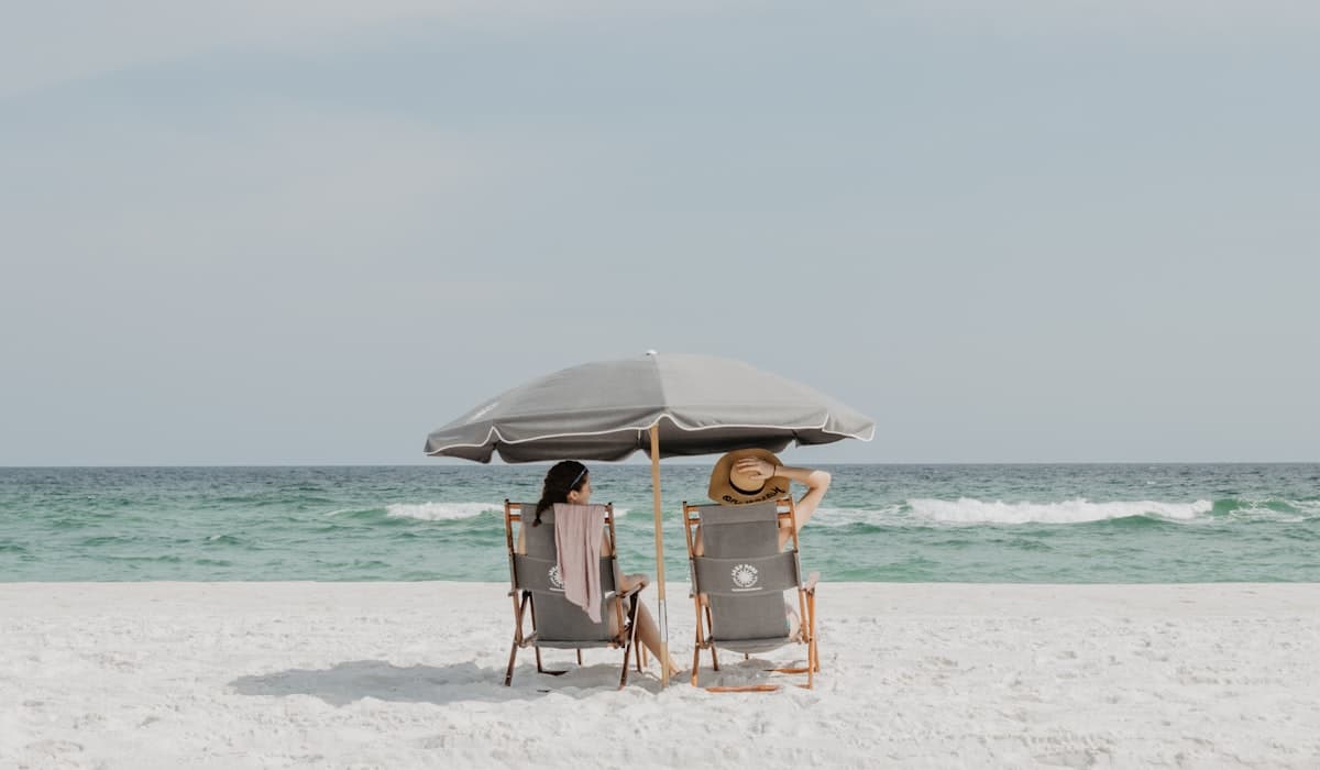 Two people sitting under a beach umbrella near the shoreline