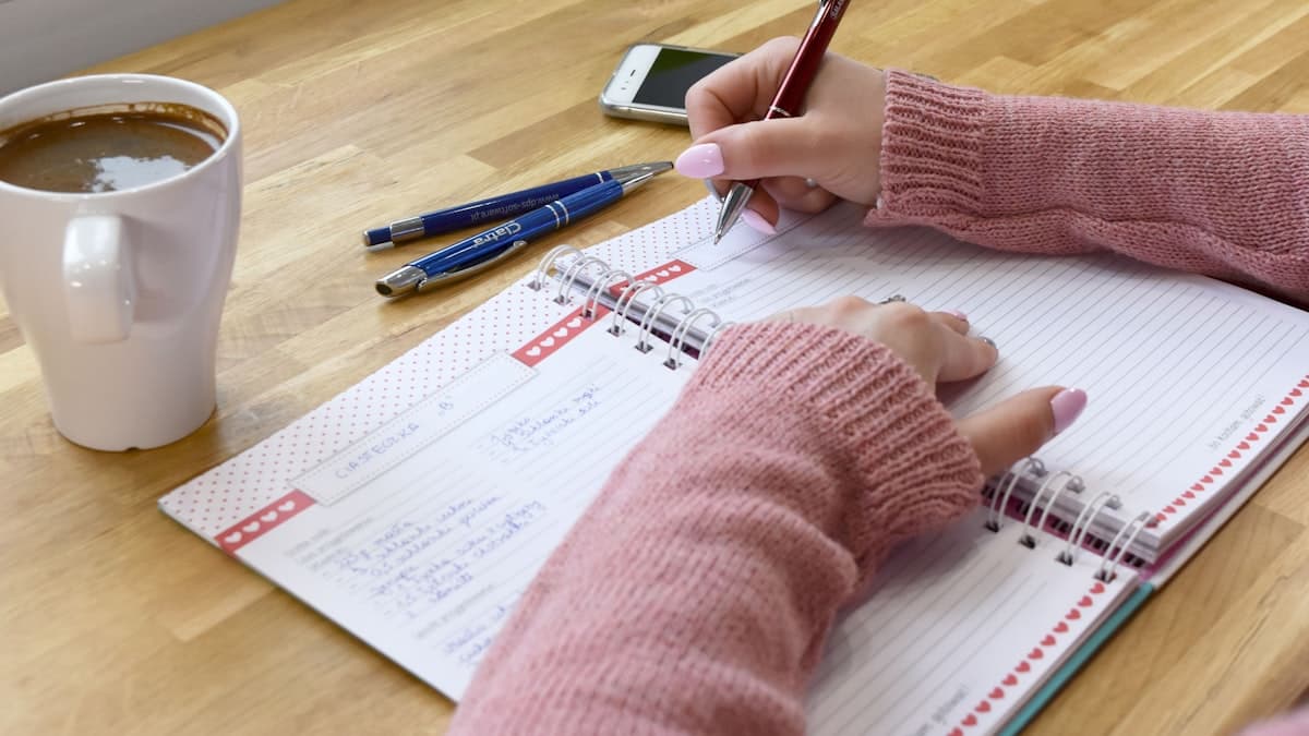 A person writing in an open notebook next to a cup of coffee, sorting thoughts on paper