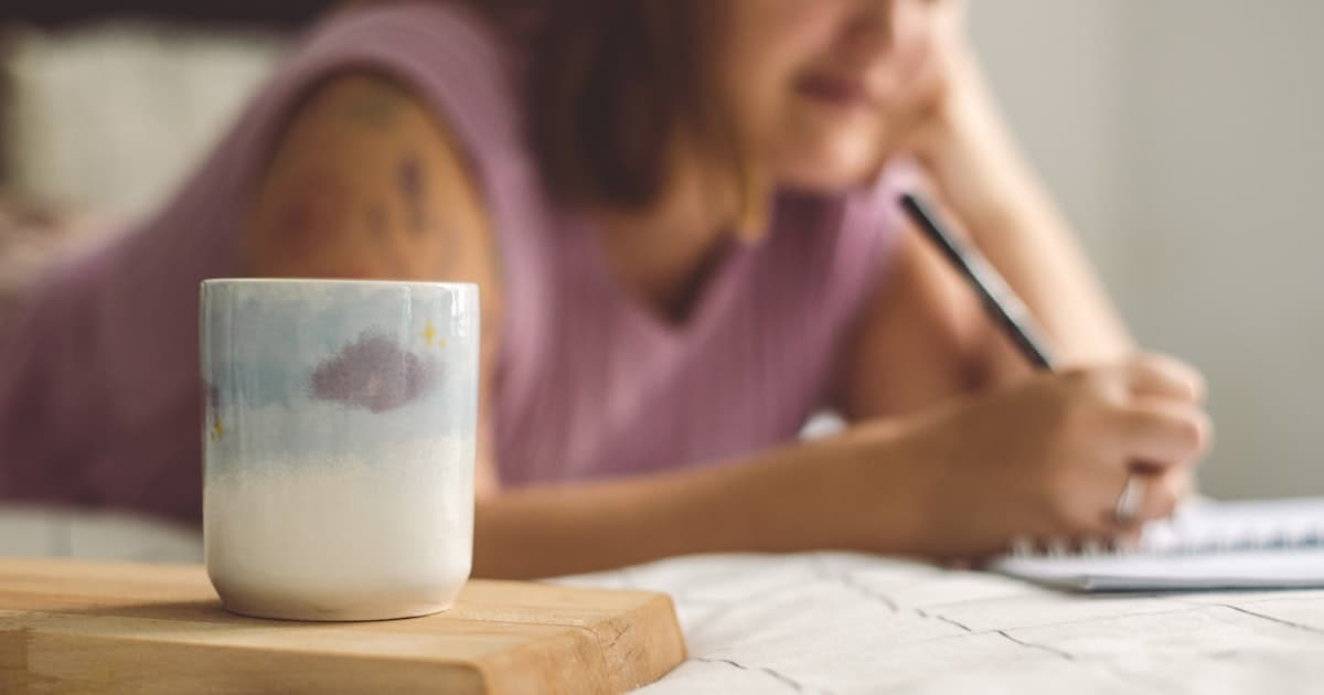 A woman writing in a notebook next to a cup of coffee — a calm weekly finance check-in