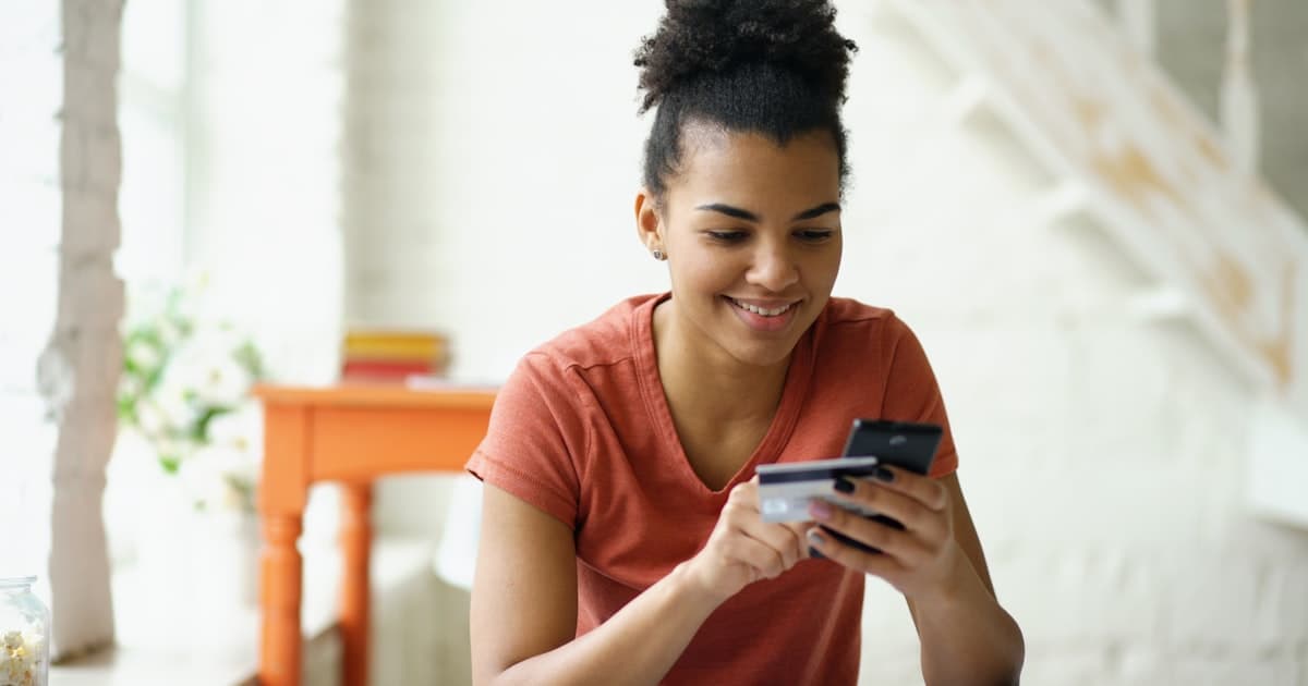 Young woman smiling while holding a credit card and checking her phone