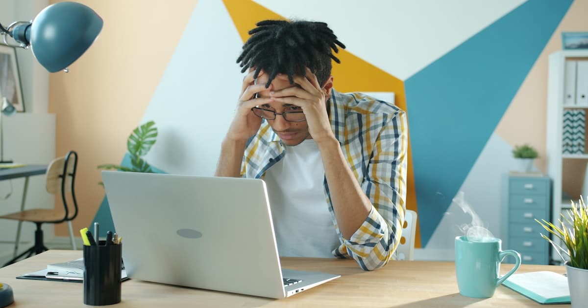 Man holding his head in frustration while sitting in front of a laptop