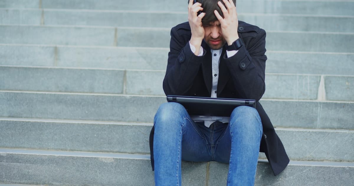 A man sitting on steps with his head in his hands, looking overwhelmed