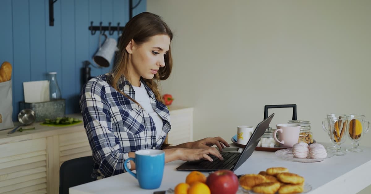Woman working on a laptop in a bright kitchen during breakfast