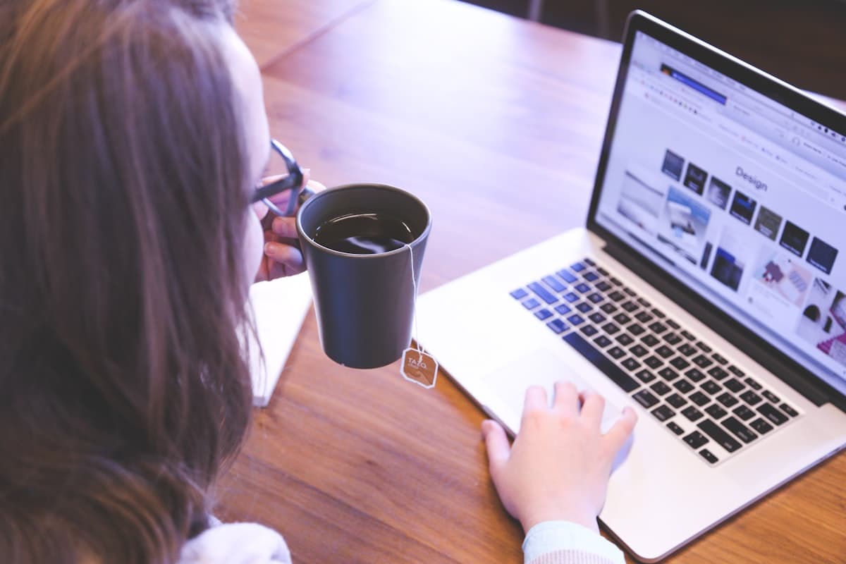 Woman holding a mug while working calmly on a MacBook — the kind of relaxed, confident financial check-in you want