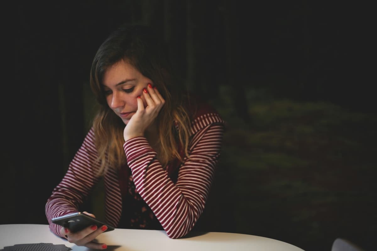 Woman leaning on table looking at her phone with a frustrated or uncertain expression