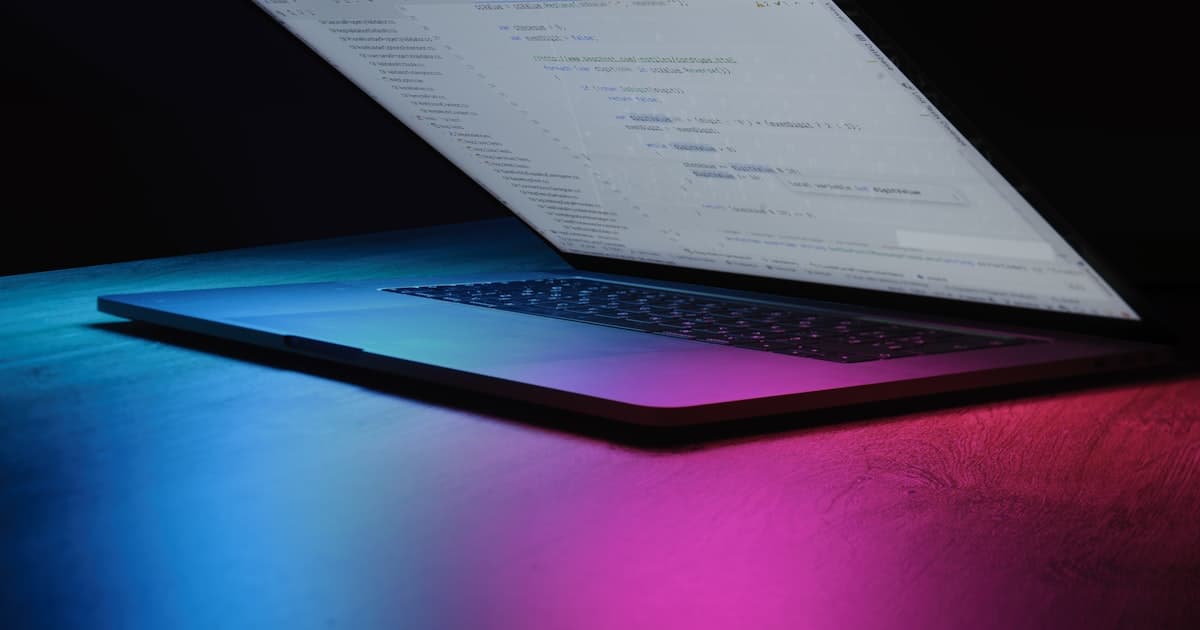 Open laptop displaying code with neon lighting in a dark room