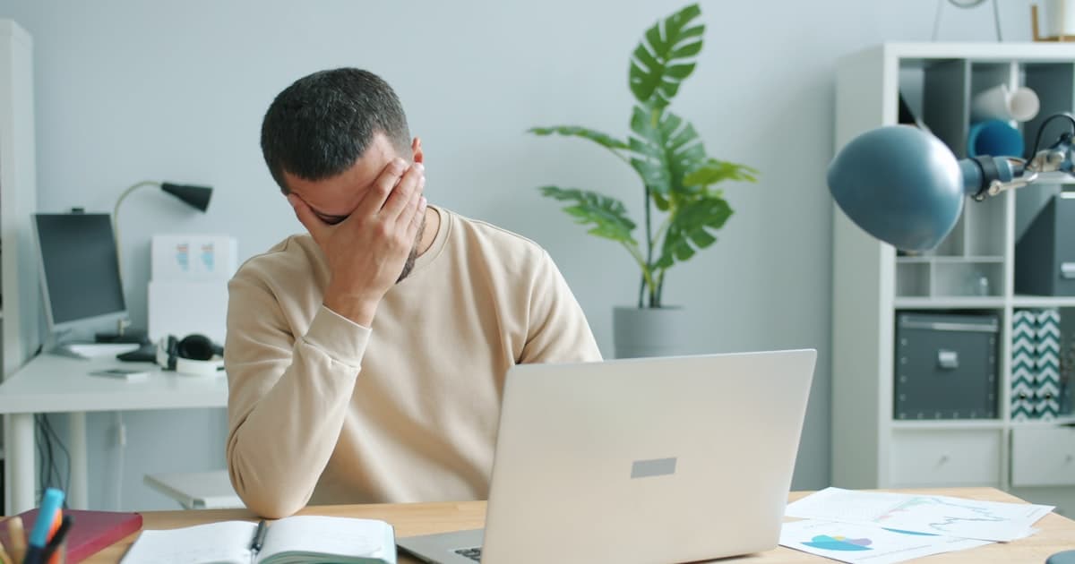 man rubbing his face in front of a laptop, overwhelmed