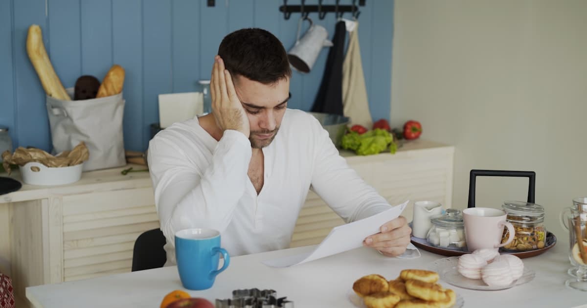 upset young man reading an unpaid bill at a kitchen table in the morning