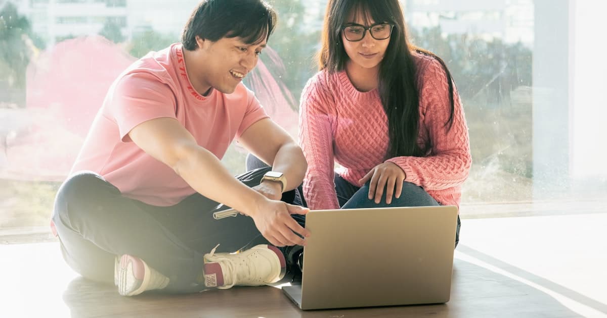A man and woman sitting on the floor together, looking at a laptop